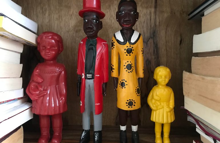 Red and yellow plastic Clonette Dolls stand alongside Ghanaian wooden figures